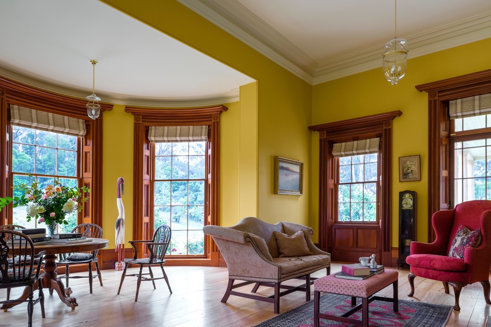 Idée de décoration pour un grand salon tradition fermé avec une salle de réception, un mur jaune, un sol en bois brun, une cheminée standard, un manteau de cheminée en pierre et un téléviseur dissimulé.