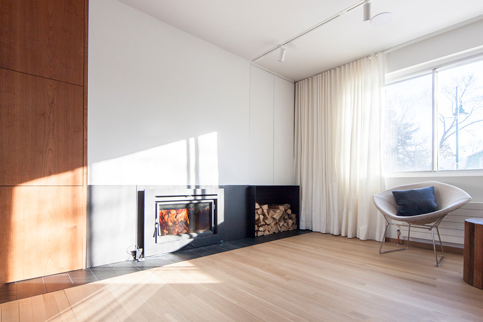 Mittelgroßes, Offenes Modernes Wohnzimmer mit weißer Wandfarbe, hellem Holzboden, Kamin, Kaminumrandung aus Metall, verstecktem TV und schwarzem Boden in Montreal