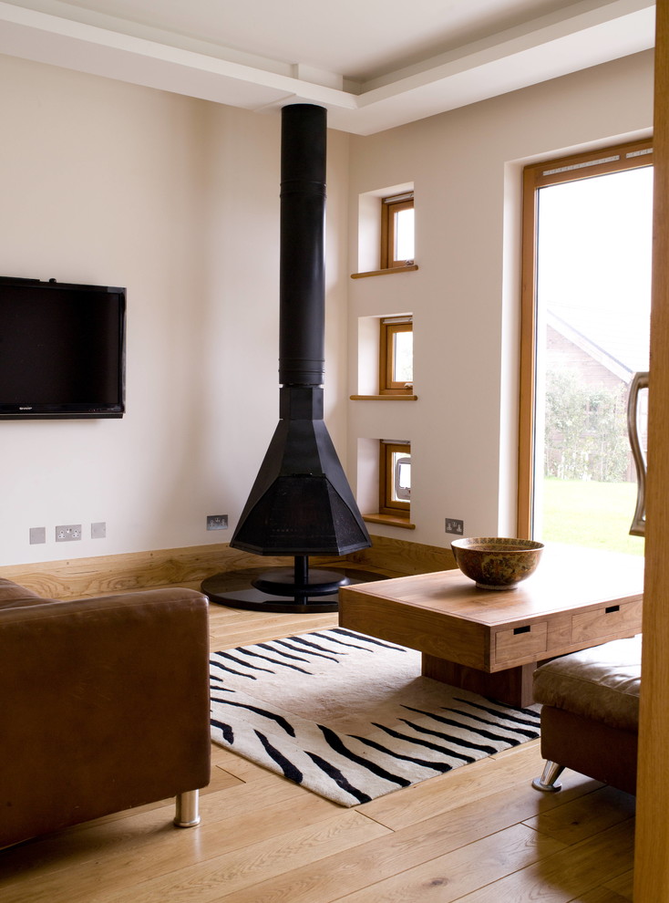 Modernes Wohnzimmer mit beiger Wandfarbe, braunem Holzboden und Hängekamin in Kanalinseln