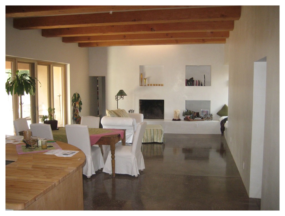 Imagen de salón abierto contemporáneo de tamaño medio con paredes beige, suelo de cemento, todas las chimeneas, marco de chimenea de yeso y televisor retractable
