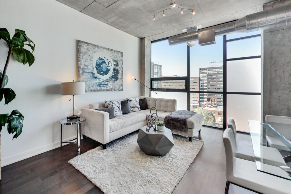 Large industrial open plan living room in Toronto with white walls, dark hardwood flooring and brown floors.