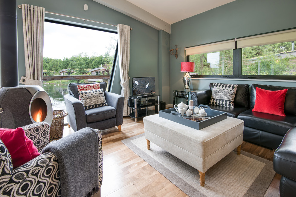 Immagine di un soggiorno eclettico di medie dimensioni e chiuso con pareti blu, parquet chiaro, stufa a legna, TV autoportante e cornice del camino in cemento