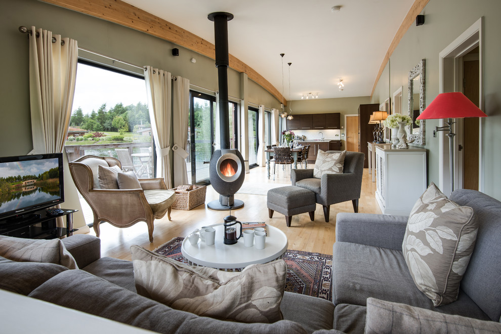 Diseño de salón abierto bohemio grande con paredes verdes, suelo de madera clara, estufa de leña y televisor independiente