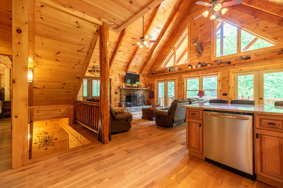 Aménagement d'un salon montagne ouvert avec un sol en bois brun, une cheminée standard et un manteau de cheminée en pierre.