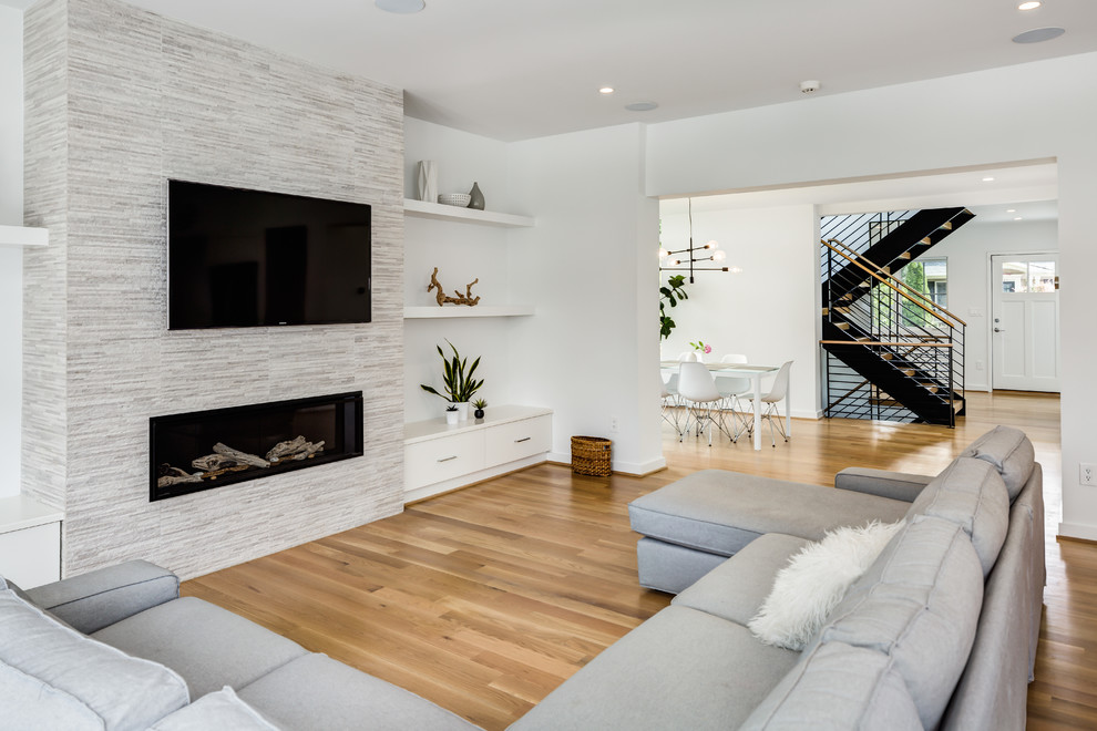 Large modern open plan living room in DC Metro with white walls, light hardwood flooring, a ribbon fireplace, a stone fireplace surround, a wall mounted tv and beige floors.