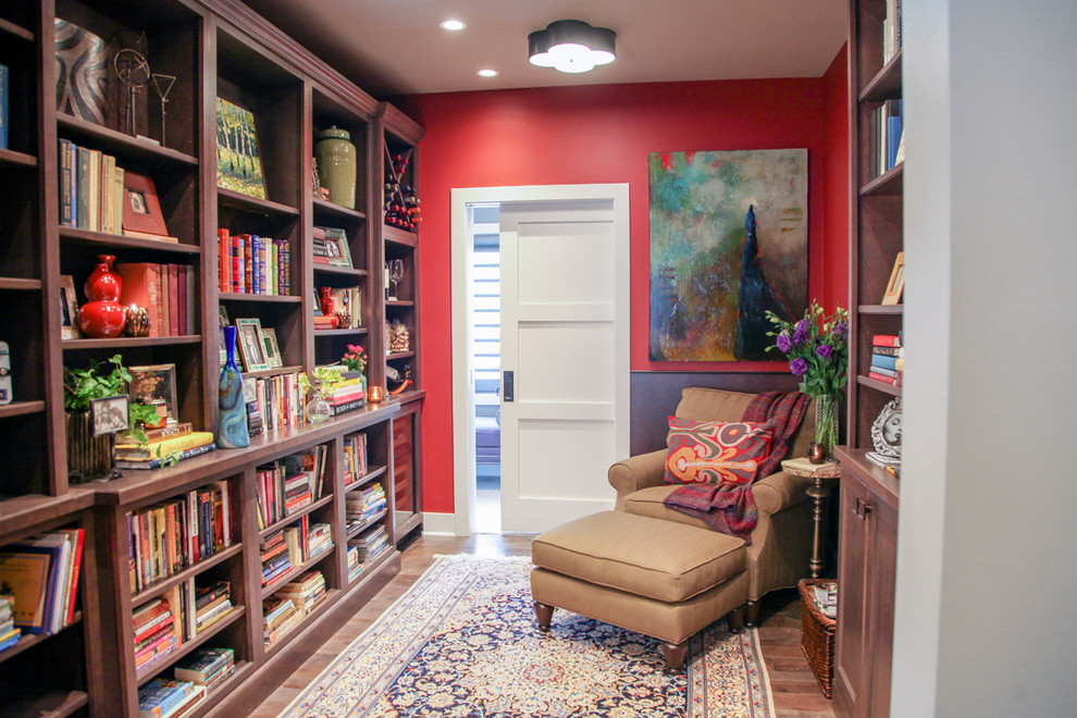 Cette image montre un petit salon bohème fermé avec une bibliothèque ou un coin lecture, un mur rouge, un sol en bois brun, aucune cheminée, un manteau de cheminée en pierre et aucun téléviseur.