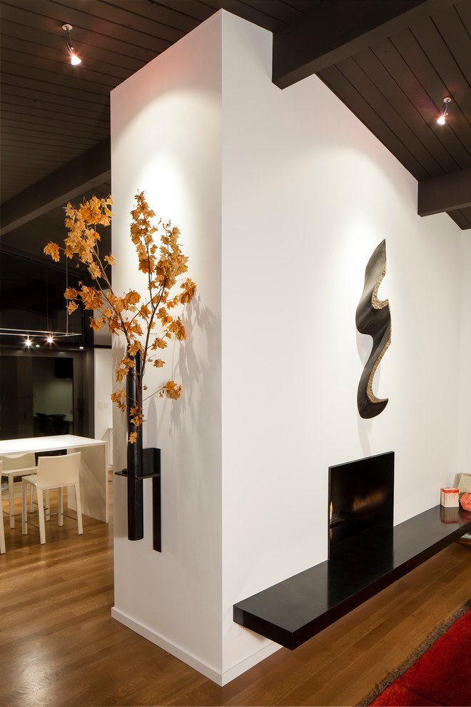 Réalisation d'un salon design ouvert avec un mur blanc, un sol en bois brun, une cheminée double-face et un manteau de cheminée en métal.