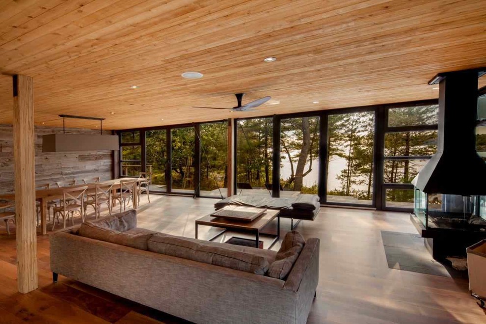 Diseño de salón minimalista con suelo de madera en tonos medios, chimenea de doble cara y marco de chimenea de madera