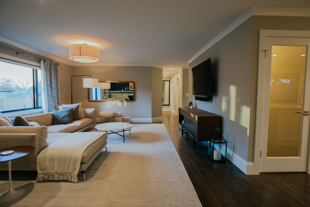 На фото: огромная открытая гостиная комната в стиле неоклассика (современная классика) с серыми стенами, паркетным полом среднего тона, угловым камином, фасадом камина из камня, телевизором на стене и коричневым полом