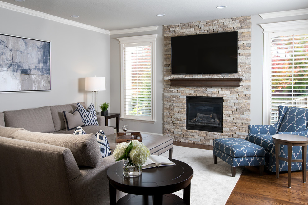 Пример оригинального дизайна: большая изолированная гостиная комната в стиле неоклассика (современная классика) с серыми стенами, стандартным камином, фасадом камина из камня, телевизором на стене и паркетным полом среднего тона