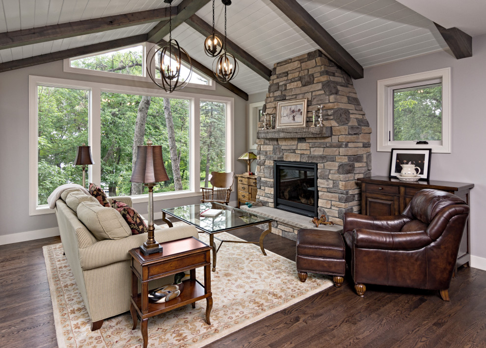 Cette image montre un salon traditionnel avec une salle de réception, un mur gris, un sol en bois brun, une cheminée standard, un manteau de cheminée en pierre, aucun téléviseur et un sol marron.