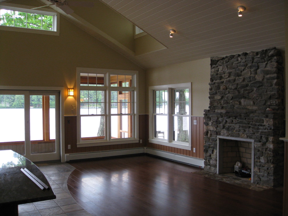 Idéer för att renovera ett litet amerikanskt vardagsrum, med gula väggar, mörkt trägolv, en standard öppen spis och en spiselkrans i sten