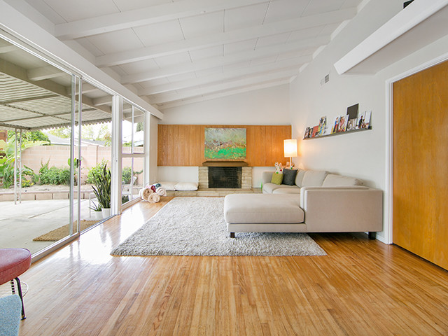 Offenes Mid-Century Wohnzimmer mit weißer Wandfarbe, hellem Holzboden, Kamin und Kaminumrandung aus Stein in Orange County