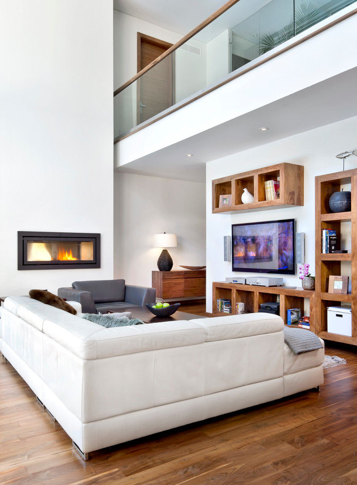 Cette image montre un salon design ouvert avec un mur blanc, un sol en bois brun, une cheminée ribbon et un téléviseur fixé au mur.