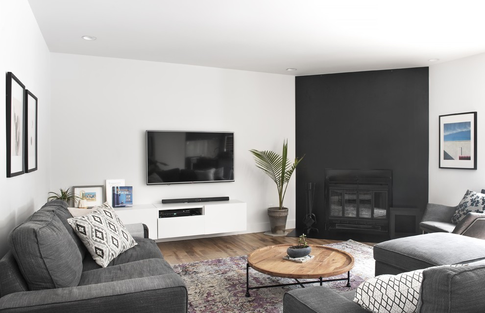 Ejemplo de salón abierto moderno de tamaño medio con paredes blancas, suelo de madera en tonos medios, chimenea de esquina, marco de chimenea de metal, televisor colgado en la pared y suelo negro
