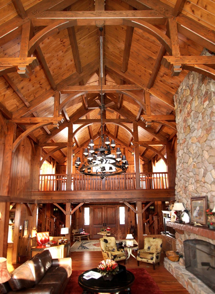 Cette photo montre un grand salon montagne ouvert avec une salle de réception, un sol en bois brun, une cheminée standard, un manteau de cheminée en pierre, aucun téléviseur et un sol marron.