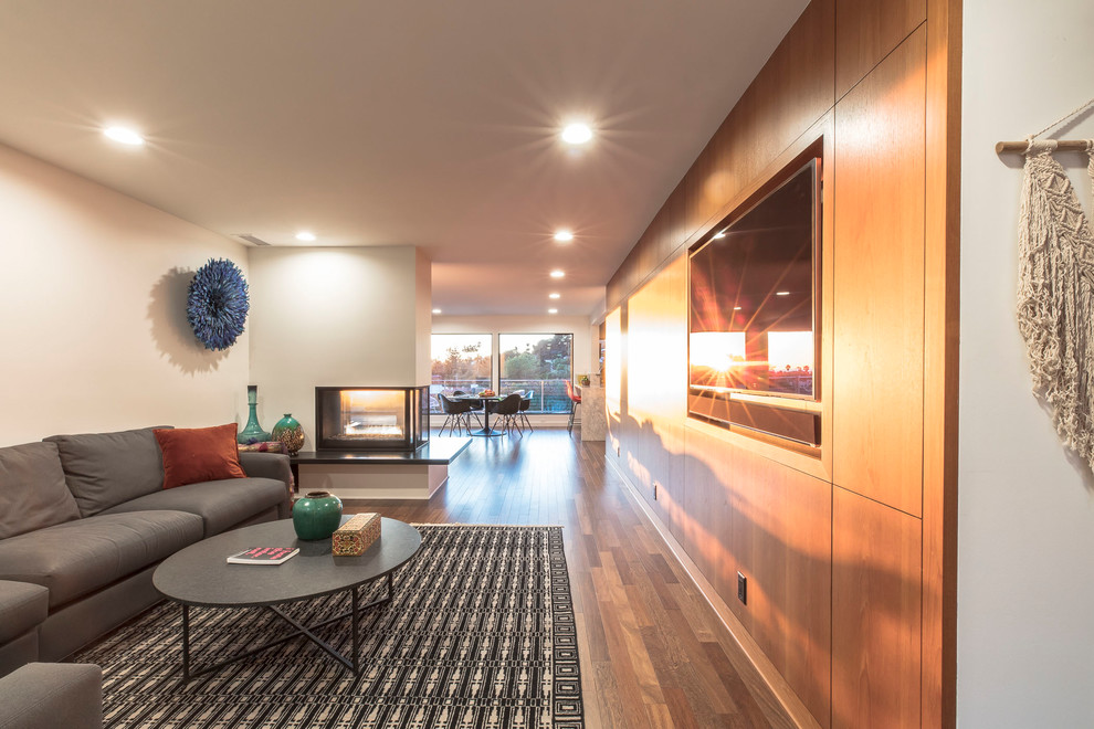Mittelgroßes, Offenes Modernes Wohnzimmer mit weißer Wandfarbe, braunem Holzboden, Tunnelkamin, Kaminumrandung aus Metall und Multimediawand in Los Angeles