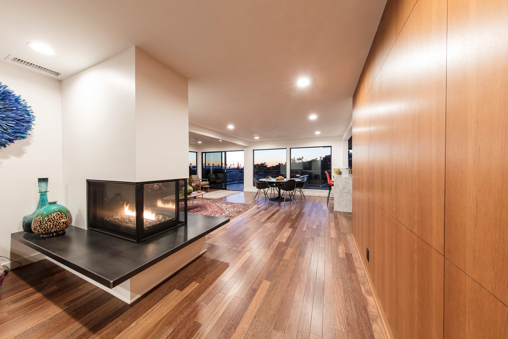 This is an example of a medium sized contemporary open plan living room in Los Angeles with white walls, medium hardwood flooring, a two-sided fireplace, a metal fireplace surround and a built-in media unit.