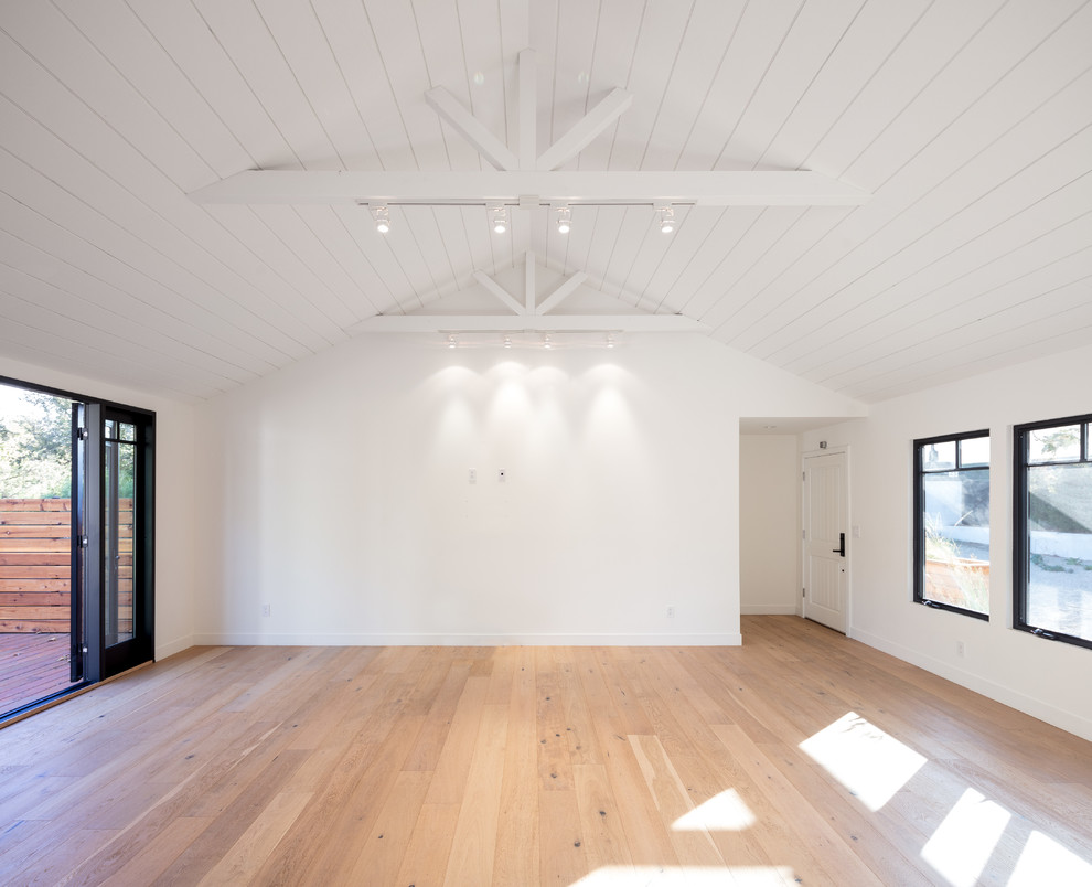 Modelo de salón abierto de estilo de casa de campo de tamaño medio con paredes blancas, suelo de madera clara y televisor colgado en la pared