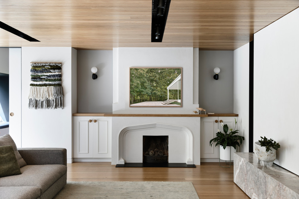 Modelo de salón para visitas abierto grande con paredes blancas, suelo de madera clara, todas las chimeneas, marco de chimenea de yeso y suelo marrón