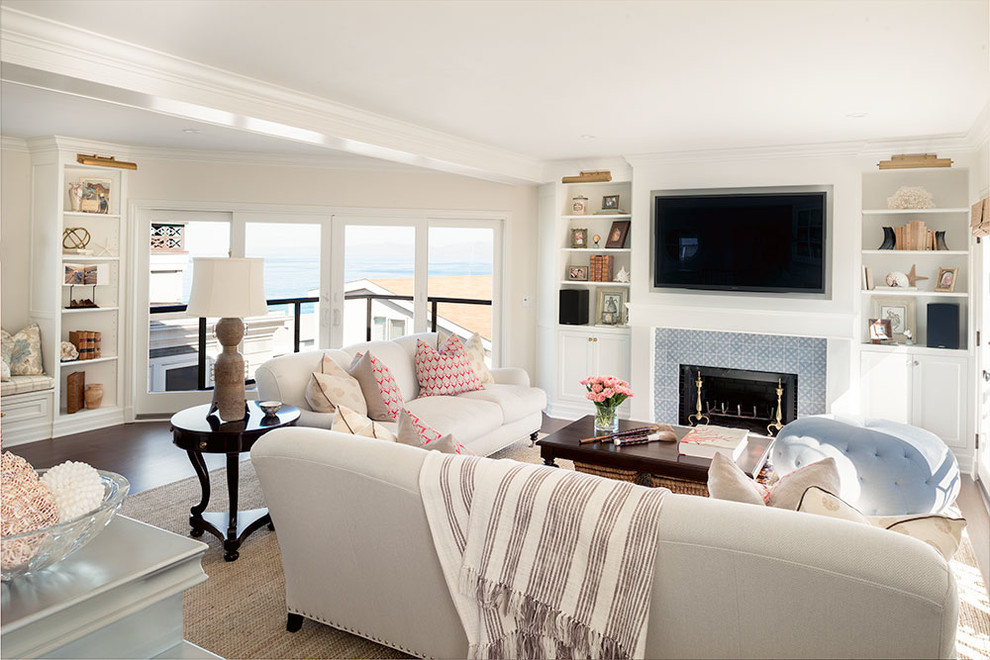 Exemple d'un grand salon bord de mer ouvert avec un mur beige, parquet foncé, une cheminée standard, un manteau de cheminée en carrelage et un téléviseur fixé au mur.