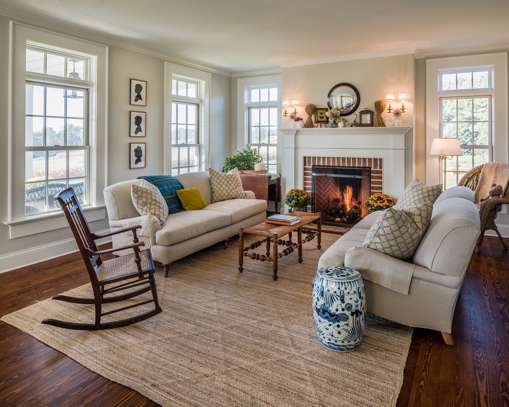 This is an example of a country living room in Philadelphia with beige walls, dark hardwood flooring, a standard fireplace, a brick fireplace surround, brown floors and feature lighting.