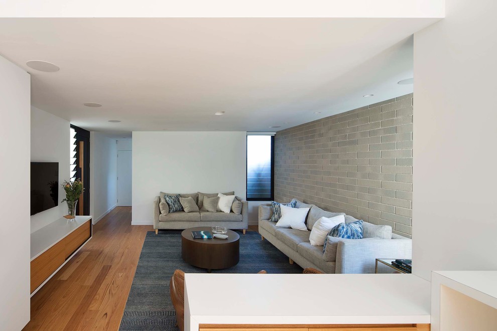 Imagen de salón abierto minimalista sin chimenea con paredes blancas, suelo de madera en tonos medios y televisor colgado en la pared
