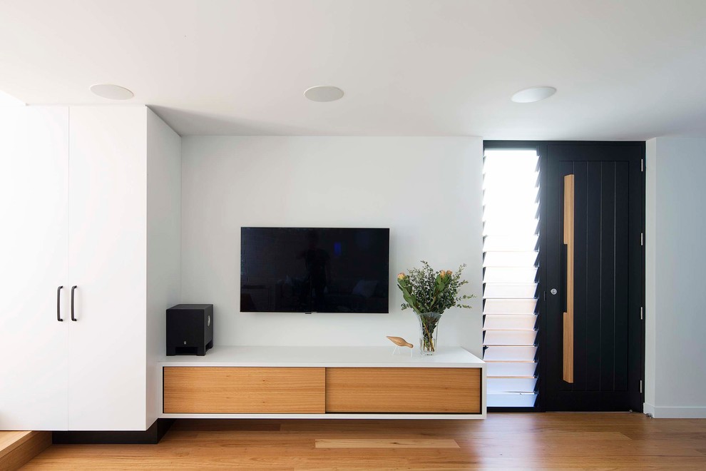 Modelo de salón abierto minimalista sin chimenea con paredes blancas, suelo de madera en tonos medios y televisor colgado en la pared