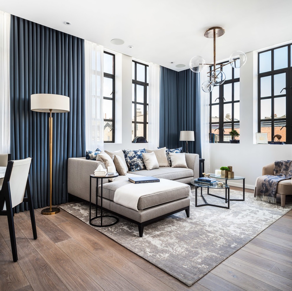 Стильный дизайн: открытая гостиная комната в современном стиле с белыми стенами, паркетным полом среднего тона и синими шторами - последний тренд
