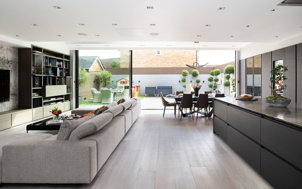Diseño de salón abierto contemporáneo extra grande sin chimenea con paredes grises, suelo de madera clara, televisor colgado en la pared y suelo beige