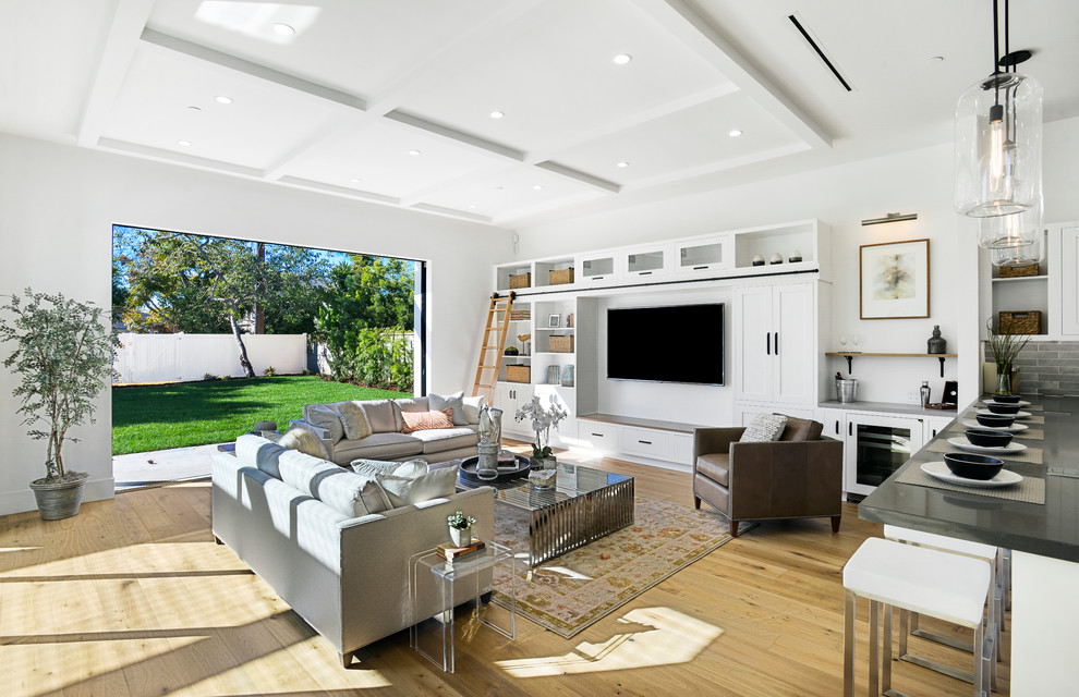 This is an example of a large farmhouse open plan living room in Los Angeles with a home bar, medium hardwood flooring, a built-in media unit, white walls and brown floors.