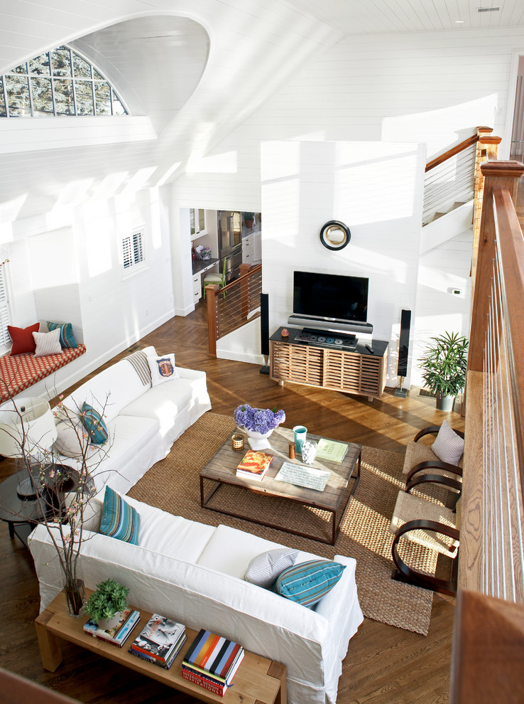 Diseño de salón abierto costero grande con paredes blancas, suelo de madera en tonos medios y televisor colgado en la pared
