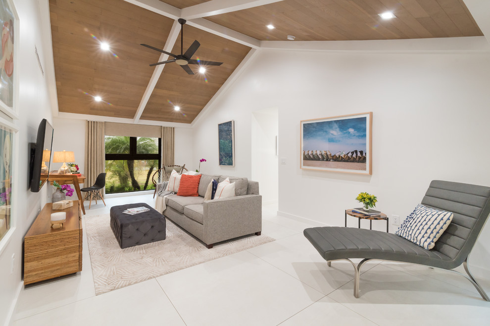 This is an example of a medium sized coastal open plan living room with white walls, porcelain flooring, a wall mounted tv and white floors.
