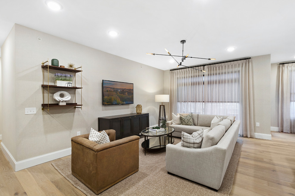 This is an example of a classic open plan living room in New York with beige walls, light hardwood flooring, a wall mounted tv and brown floors.