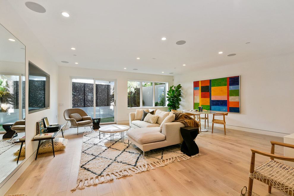 This is an example of a contemporary open plan living room in San Francisco with white walls, light hardwood flooring, a wall mounted tv and beige floors.