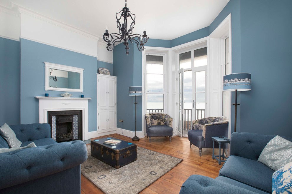 Idée de décoration pour un grand salon marin ouvert avec un mur bleu, un sol en bois brun, une cheminée standard, un manteau de cheminée en carrelage, aucun téléviseur et un sol marron.