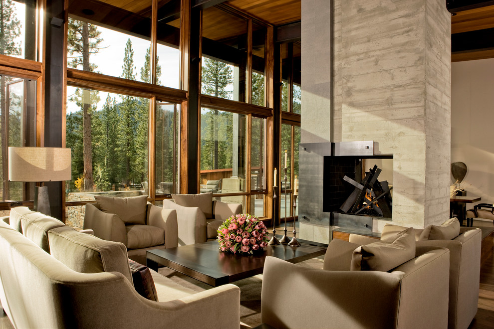 Inspiration pour un grand salon chalet ouvert avec un mur beige, un sol en bois brun, une cheminée double-face et un manteau de cheminée en béton.