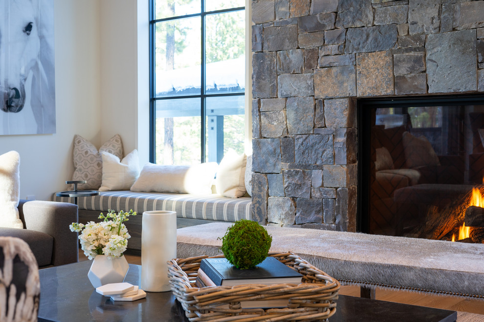 Modelo de salón abierto de estilo de casa de campo con paredes blancas, suelo de madera clara, todas las chimeneas, marco de chimenea de piedra y televisor colgado en la pared