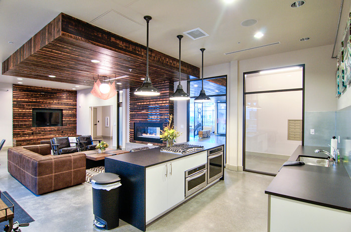 Example of an urban open concept concrete floor living room design in Portland with white walls, a two-sided fireplace, a wood fireplace surround and a media wall