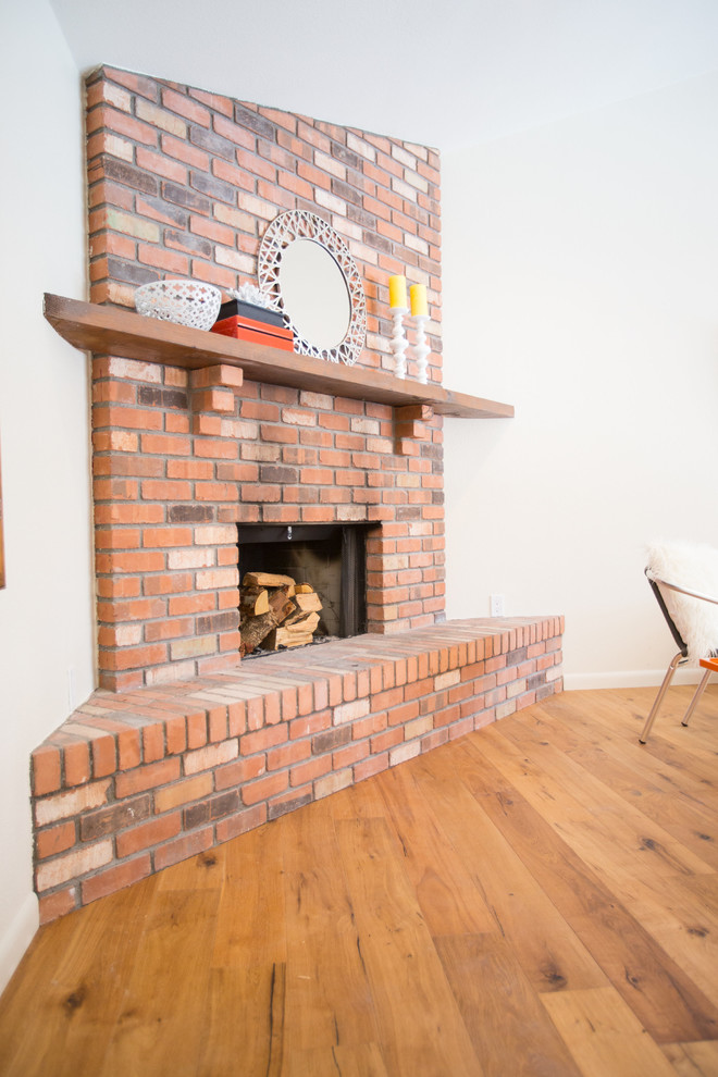 Cette photo montre un salon tendance de taille moyenne et ouvert avec un mur blanc, un sol en bois brun, une cheminée d'angle, un manteau de cheminée en brique, un téléviseur fixé au mur et un sol marron.