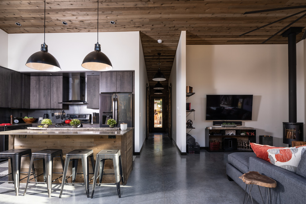 Immagine di un piccolo soggiorno industriale aperto con pareti bianche, pavimento in cemento, stufa a legna, TV a parete, pavimento grigio e soffitto in legno