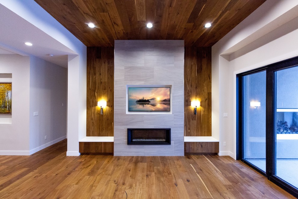 Idée de décoration pour un grand salon minimaliste ouvert avec un mur gris, un sol en bois brun, cheminée suspendue, un manteau de cheminée en carrelage, un téléviseur fixé au mur et un sol marron.