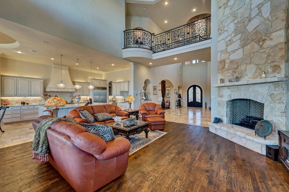 Example of a tuscan open concept dark wood floor living room design in Dallas with beige walls, a standard fireplace, a stone fireplace and a wall-mounted tv