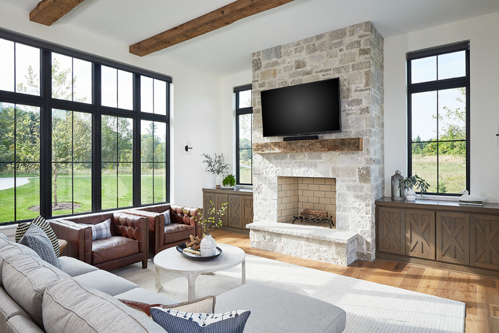 Inspiration for a farmhouse open concept brown floor, medium tone wood floor and exposed beam living room remodel in Grand Rapids with white walls, a standard fireplace, a stone fireplace and a wall-mounted tv