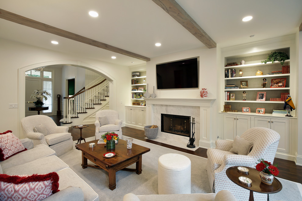 На фото: гостиная комната в классическом стиле с белыми стенами, темным паркетным полом, стандартным камином, телевизором на стене, коричневым полом и балками на потолке