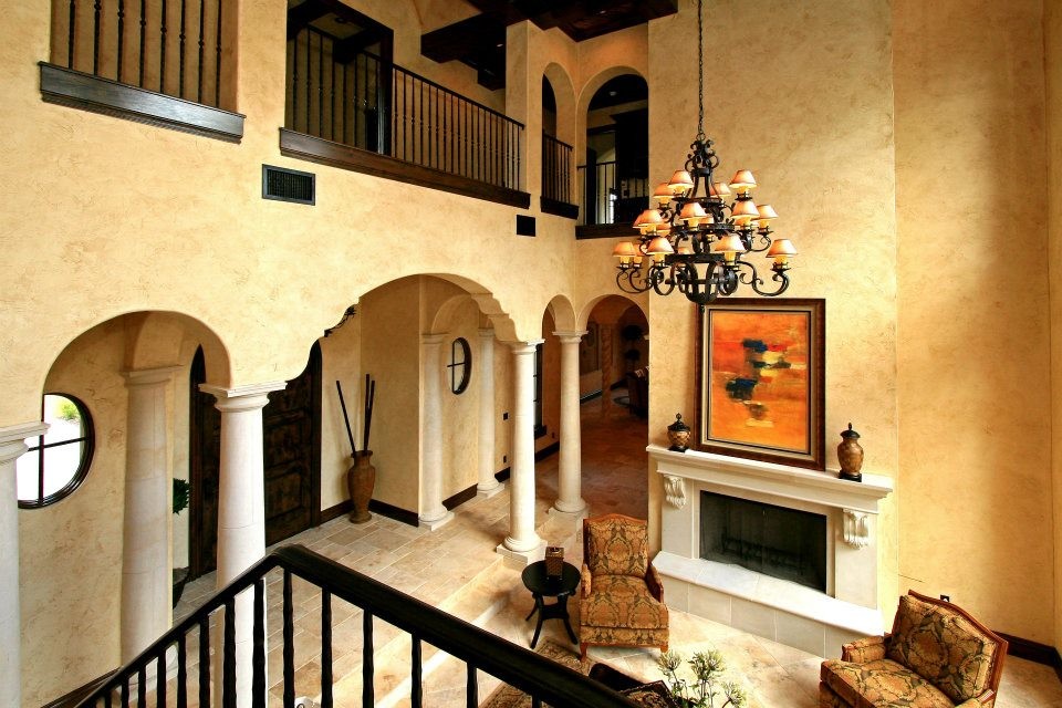 Exemple d'un grand salon mansardé ou avec mezzanine méditerranéen avec un mur beige, un sol en travertin, une cheminée standard, un manteau de cheminée en pierre, aucun téléviseur et un sol beige.