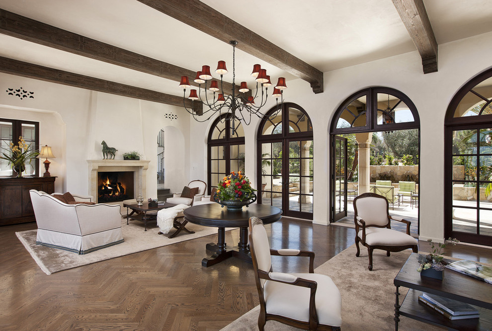 Repräsentatives Mediterranes Wohnzimmer mit beiger Wandfarbe, braunem Holzboden, Kamin, Kaminumrandung aus Stein und Rundbogen in Santa Barbara