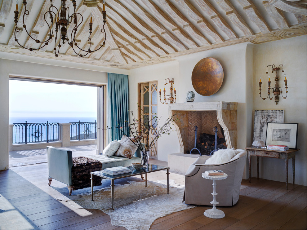 Exemple d'un très grand salon méditerranéen avec un mur blanc, un sol en bois brun, une cheminée standard, un manteau de cheminée en pierre et un sol marron.