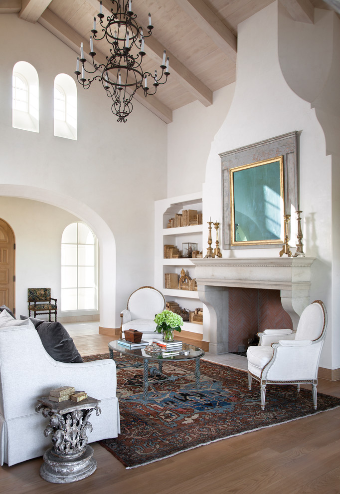 Cette image montre un salon méditerranéen avec un mur blanc, un sol en bois brun et une cheminée standard.