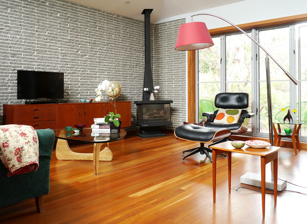 1960s medium tone wood floor living room photo in Melbourne with white walls, a wood stove and a tv stand